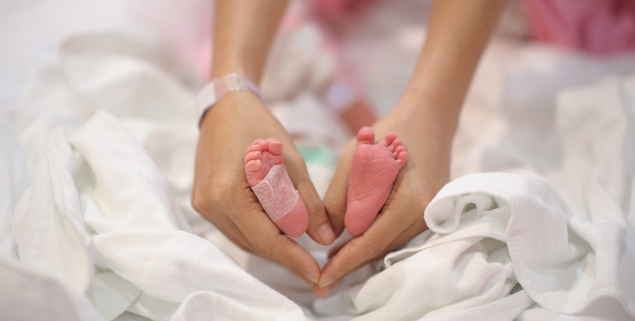 Newborn awaits protective covering for feet.