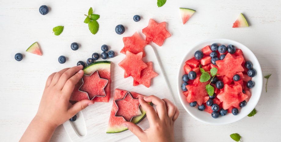 Watermelon and blueberry salad. Slices of watermelon in the shape of a star. Children's hands shaping watermelon on white table