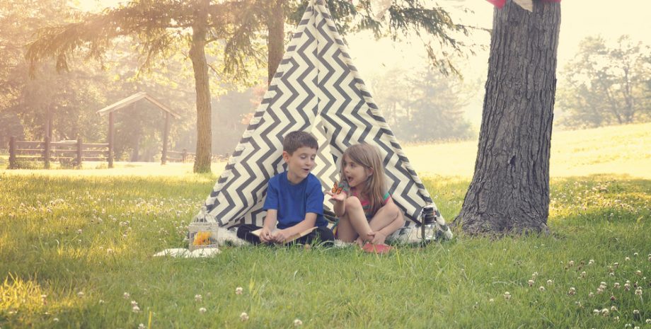 Two children sitting in a tent teepee and holding a butterfly with a nature summertime background