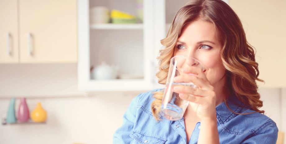 Woman standing in a modern kitchen drinking a glass of water