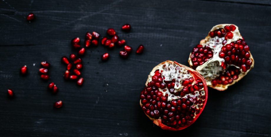 Pomegranate sliced open with loose pomegranate seeds next to it