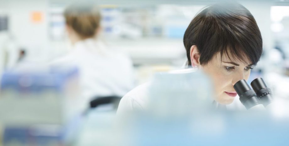 female scientist in a busy research lab looking into microscope