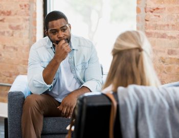 Exhausted mid adult man listens to unrecognizable female therapist