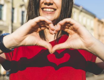Woman's hands shaping heart, shadow on red t-shirt