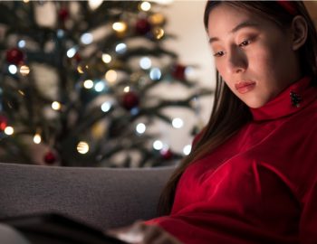 A woman on her laptop seated in front of a Christmas tree.