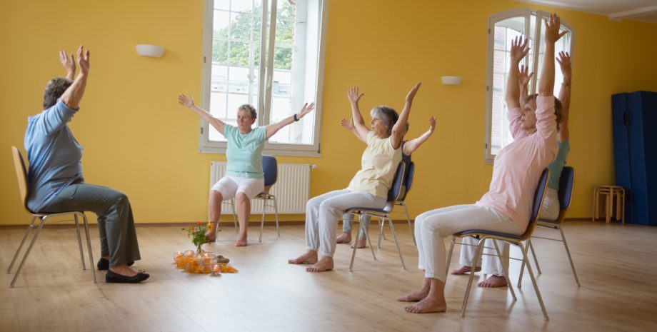 A group sitting in chairs practicing yoga poses.