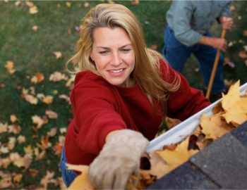 Woman cleaning her gutters on top of a ladder.