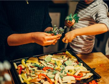 Two people sharing vegetables over a tray of assorted healthy foods.