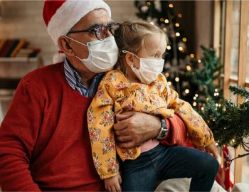 Older parent holding child while they both wear facemasks.