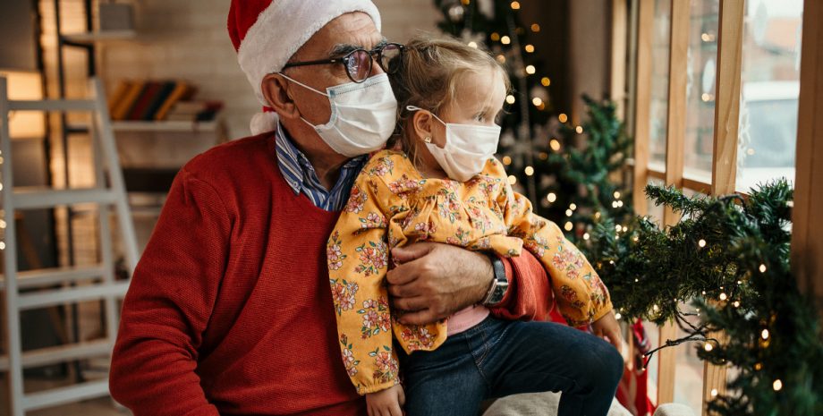 Older parent holding child while they both wear facemasks.