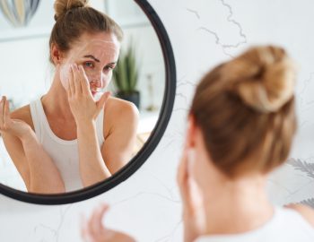 A woman applying lotion in the mirror.