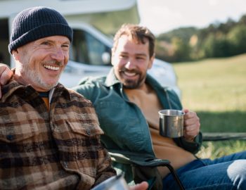 Two men sharing a drink in front of a recreational vehicle.