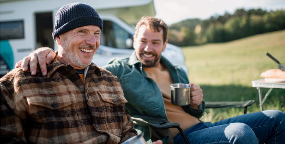 Two men sharing a drink in front of a recreational vehicle.
