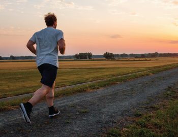A man running down a long gravel road toward a sunset.