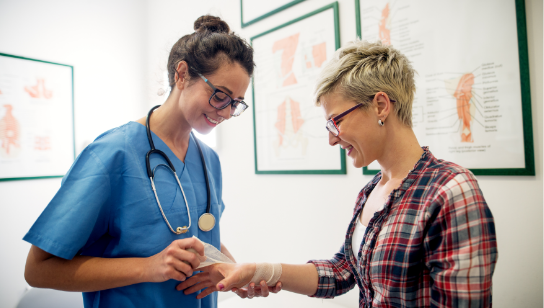 female nurse practitioner wrapping the wound of a female patient in an exam room
