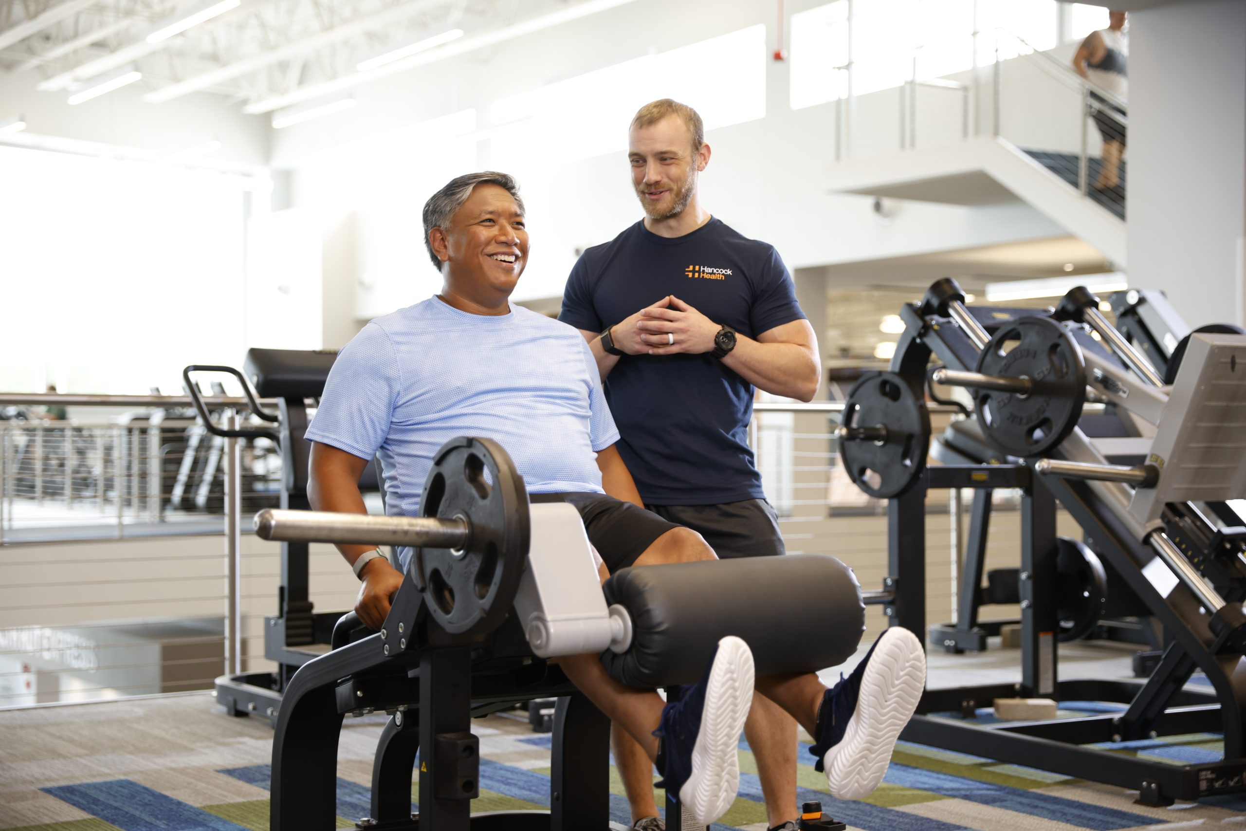 man and trainer lifting weights at a Hancock Wellness Center