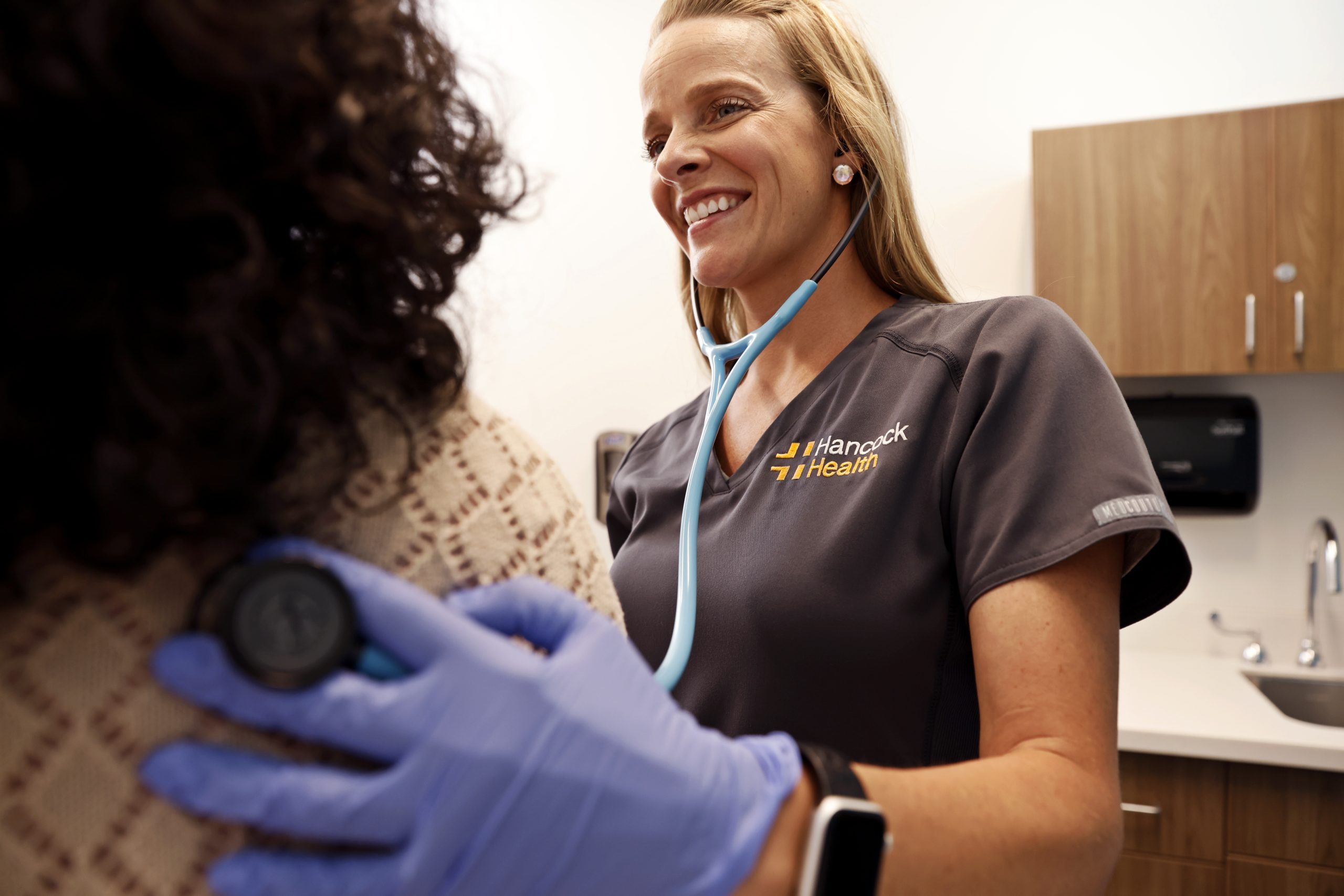 smiling nurse practitioner listening to patient's breathing with stethoscope