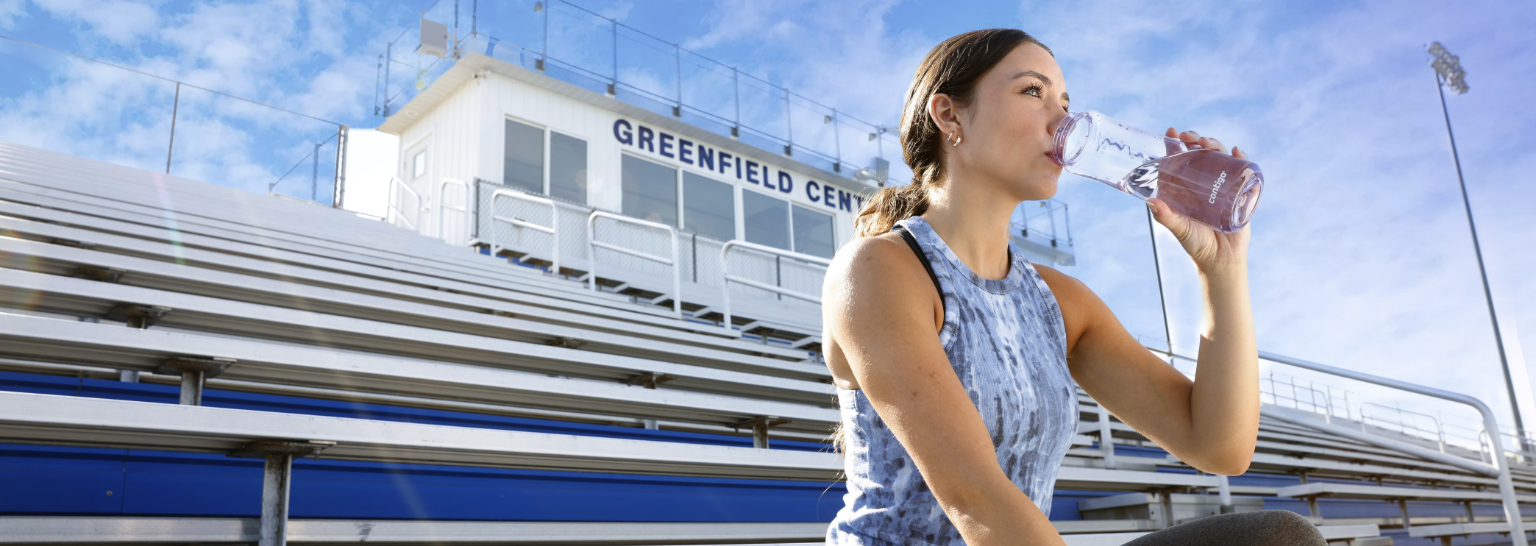 Healthy young woman drinking water in bleachers in Greenfield, Indiana