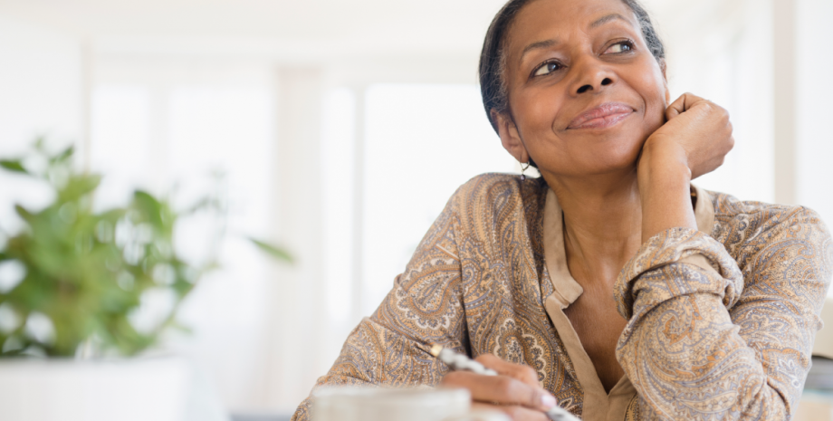 A woman writing a list and looking off to the left as she smiles.