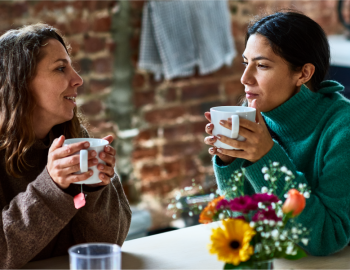 Two women having a discussion with coffee cups in their hands.