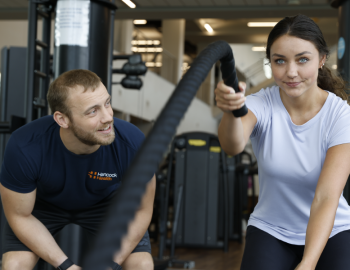 Male gym coach watching a young woman doing exercises.