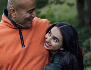 Older father hugging his younger child as they look up at him.